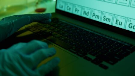hands wearing blue surgical gloves typing on a laptop